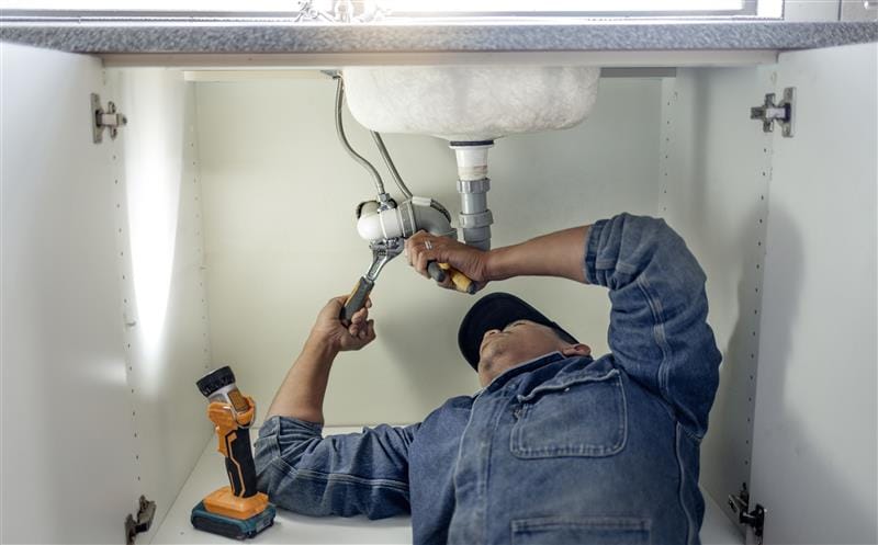 Plumber repairing pipes beneath a bathroom sink in Thornton