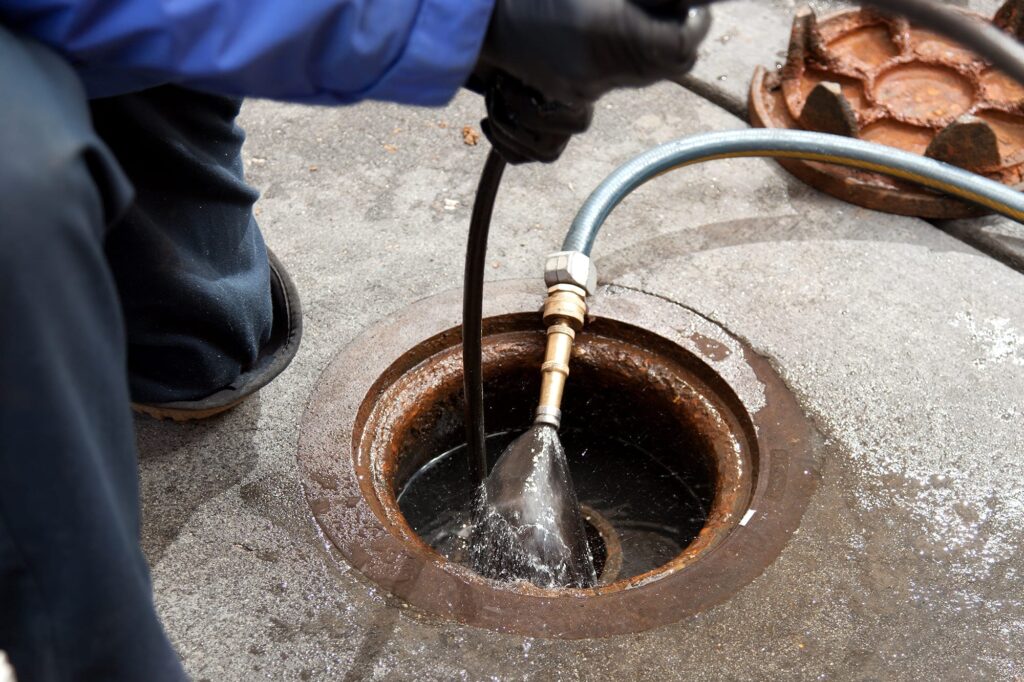 Plumber hydro jetting a sewer line through a manhole in Thornton
