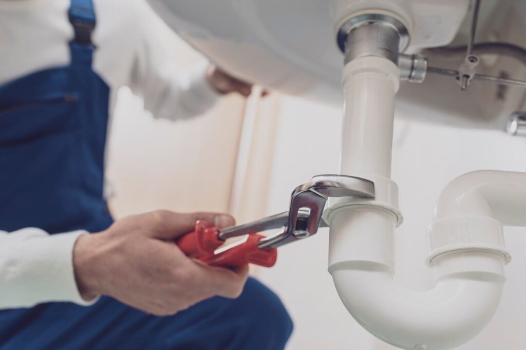 Plumber repairing a white drain pipe beneath a sink in Thornton