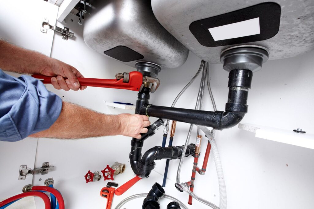 Plumber repairing drain pipes beneath a kitchen sink in Thornton